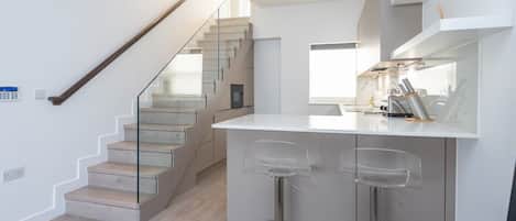 Une cuisine moderne dotée d’un îlot central, de tabourets de bar et d’un escalier menant à un niveau supérieur.