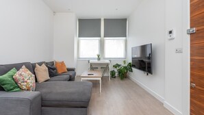 Ein modernes Wohnzimmer mit einem grauen Sofa, einem kleinen Couchtisch und einem an der Wand befestigten Fernseher.