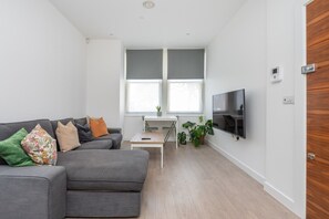 A modern living room with a grey sofa, a small coffee table, and a TV mounted on the wall. - Fulham Duplex Near Parsons Green Station (London)