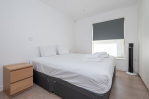 A minimalist bedroom with a bed, bedside table, and a standing heater. - Fulham Duplex Near Parsons Green Station (London)