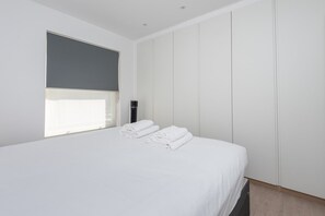A modern hotel room with a large bed, a window with blinds, and a wardrobe. - Fulham Duplex Near Parsons Green Station (London)