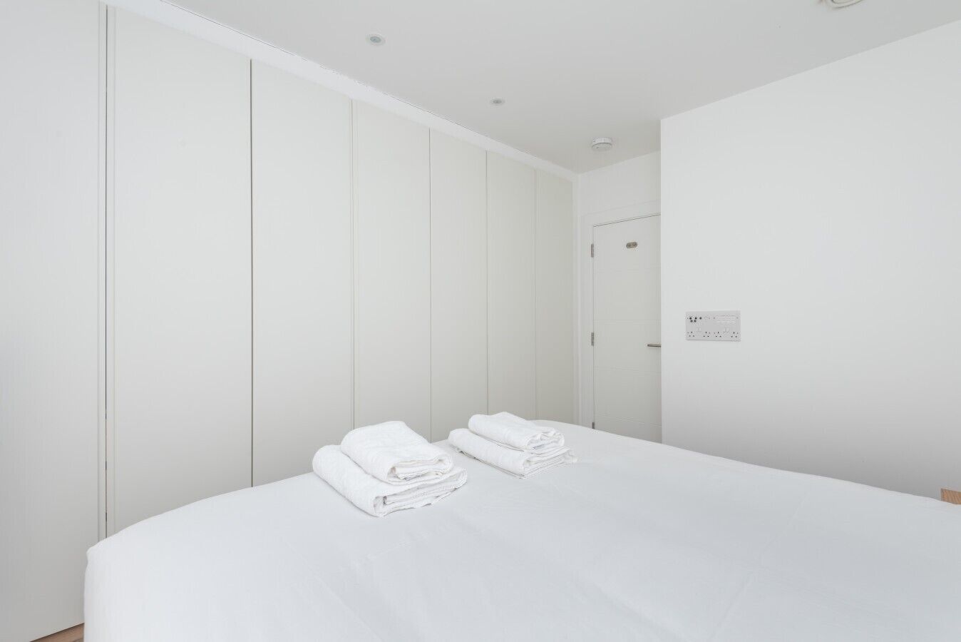 Quarto de hotel com uma cama grande, um guarda-roupa e uma tomada na parede.