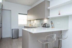 A modern kitchen with a central island, bar stools, and a stainless steel refrigerator. - Fulham Duplex Near Parsons Green Station (London)