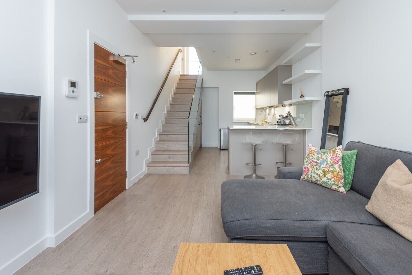A modern living room with a grey sofa, a wooden coffee table, and a staircase leading to a kitchen area.