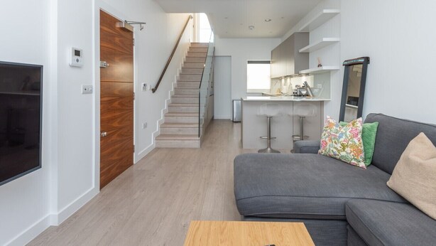 Ein modernes Wohnzimmer mit grauem Sofa, einem Holztisch und einer Treppe, die in einen Küchenbereich führt.