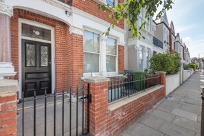 A row of terraced houses with a brick facade, white window frames, and a black metal fence. - Fulham Duplex Near Parsons Green Station (London)