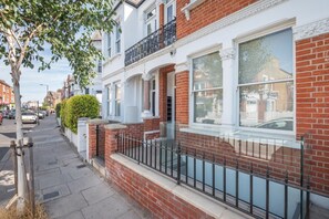 A row of terraced houses with a brick facade, white window frames, and a black metal balcony railing. - Fulham Duplex Near Parsons Green Station (London)