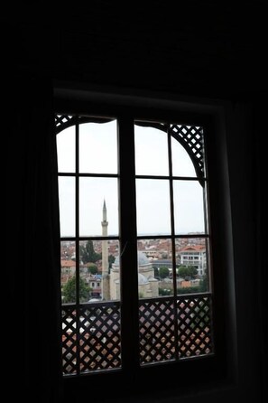 Ventana con celosía desde la cual se aprecia un paisaje urbano con una torre destacada.