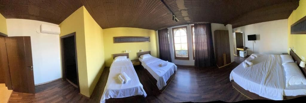 A hotel room with two single beds, a large bed, a wardrobe, a television, and a window with curtains.
