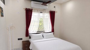Ein Hotelzimmer mit Bett, Fenster mit Vorhängen, Klimaanlage und Wandheizung.