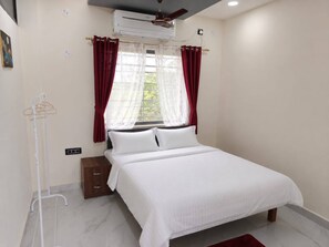 A hotel room with a bed, a window with curtains, an air conditioning unit, and a wall-mounted heater. - Evergreen Home Stay (Durgapur)
