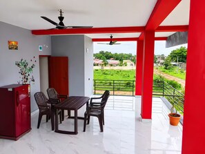 A dining area with a table and chairs, a ceiling fan, and a view of a green landscape. - Evergreen Home Stay (Durgapur)