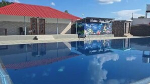 Ein Swimmingpool mit glatter, blauer Wasseroberfläche, ein Gebäude mit rotem Dach und ein Schild mit einem farbenfrohen Wandbild.