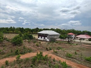 A rural landscape with a modern building, a dirt road, and surrounding greenery. - Evergreen Home Stay (Durgapur)