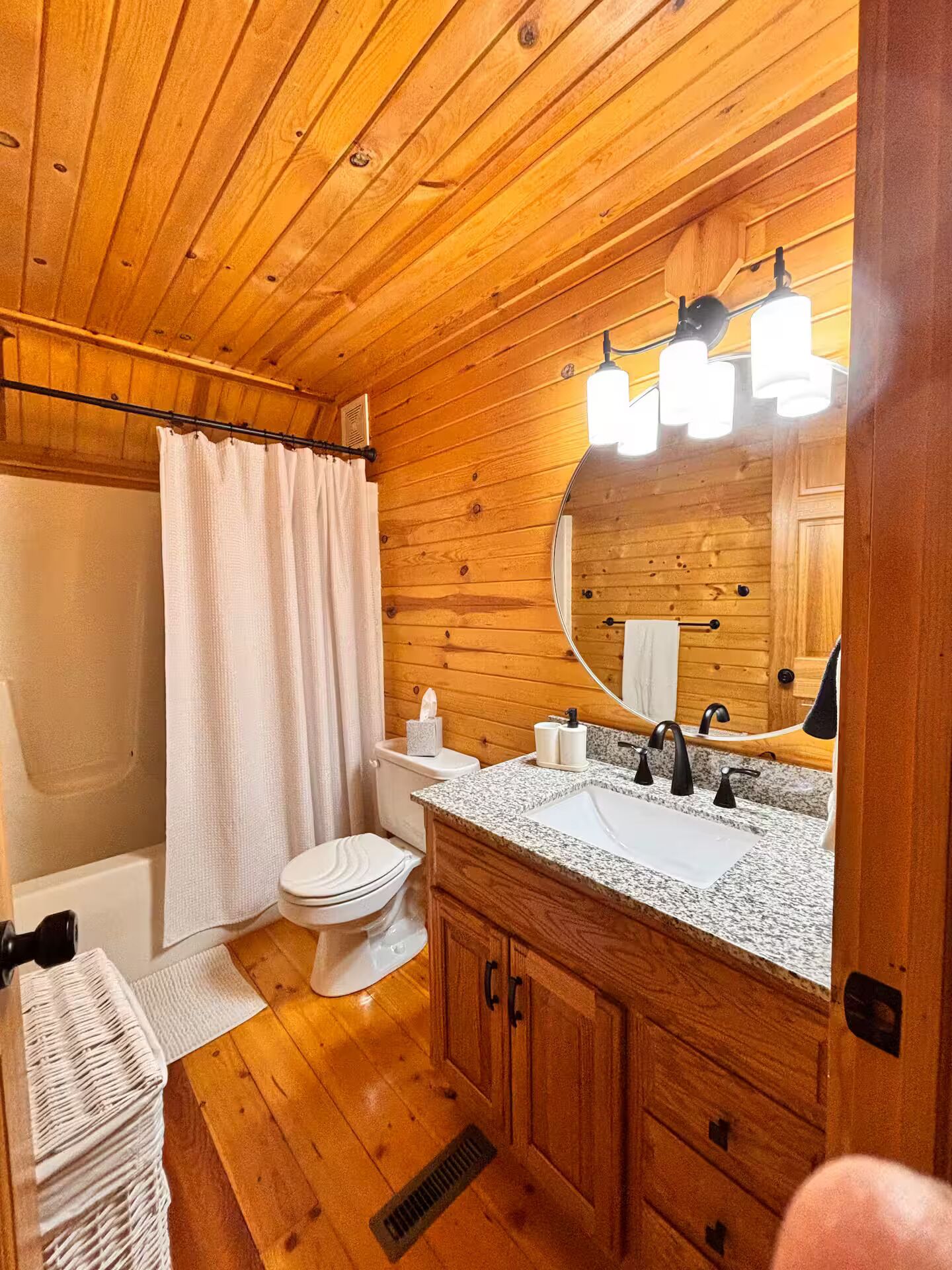 Une salle de bain rustique, aménagée dans une cabane en bois, avec douche, toilettes, lavabo et miroir.