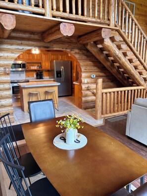 A wooden interior with a dining table, chairs, a kitchen area, and a staircase. - Charming Log Cabin in the Heart of Amish Country (Millersburg)