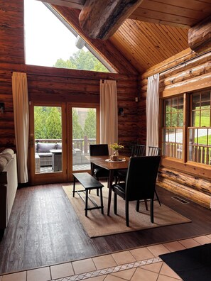 A wooden cabin interior with a dining area, a sofa, and a view through a glass door. - Charming Log Cabin in the Heart of Amish Country (Millersburg)