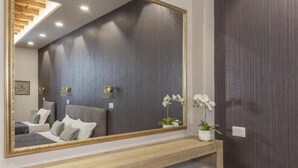 A bedroom with a large mirror, a wooden bench, a bed with pillows, and a nightstand with a plant. - SweetHouse Campo de Fiori (Roma)