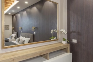 Ein Schlafzimmer mit einem großen Spiegel, einer Holzbank, einem Bett mit Kissen und einem Nachttisch mit einer Pflanze.