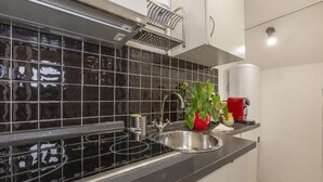 A kitchen with a black tiled backsplash, stainless steel sink, and a red kettle. - SweetHouse Campo de Fiori (Roma)