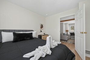 A bedroom with a bed, bedside table, lamp, and a door leading to another room.