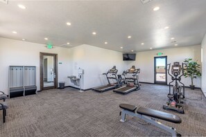 Ein Fitnessraum mit Laufbändern, einer Bank und einem an der Wand montierten Fernseher.