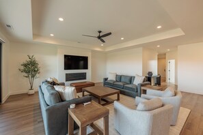 A spacious living room with a flat-screen TV, a ceiling fan, and a large potted plant. - The Approach Shot: 4  BR, 4  BA House in St. George, Sleeps 10 (St. George)