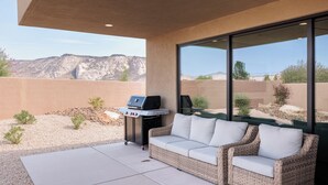 An outdoor patio with a grill, a cushioned seating area, and a view of a desert landscape. - The Approach Shot: 4  BR, 4  BA House in St. George, Sleeps 10 (St. George)