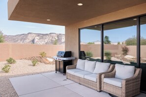 An outdoor patio with a grill, a cushioned seating area, and a view of a desert landscape. - The Approach Shot: 4  BR, 4  BA House in St. George, Sleeps 10 (St. George)