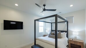A bedroom with a four-poster bed, a ceiling fan, a mounted TV, and a bedside table with a lamp. - The Approach Shot: 4  BR, 4  BA House in St. George, Sleeps 10 (St. George)