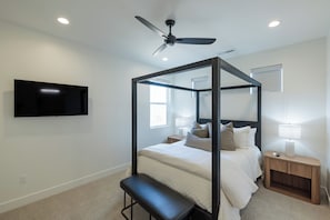 A bedroom with a four-poster bed, a ceiling fan, a mounted TV, and a bedside table with a lamp. - The Approach Shot: 4  BR, 4  BA House in St. George, Sleeps 10 (St. George)