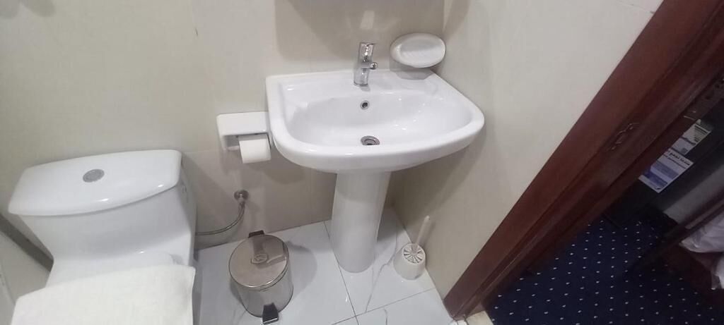 A bathroom with a toilet, sink, and a trash bin.