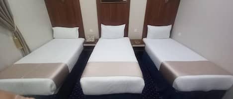 A hotel room with three single beds, each with a pillow and a nightstand.