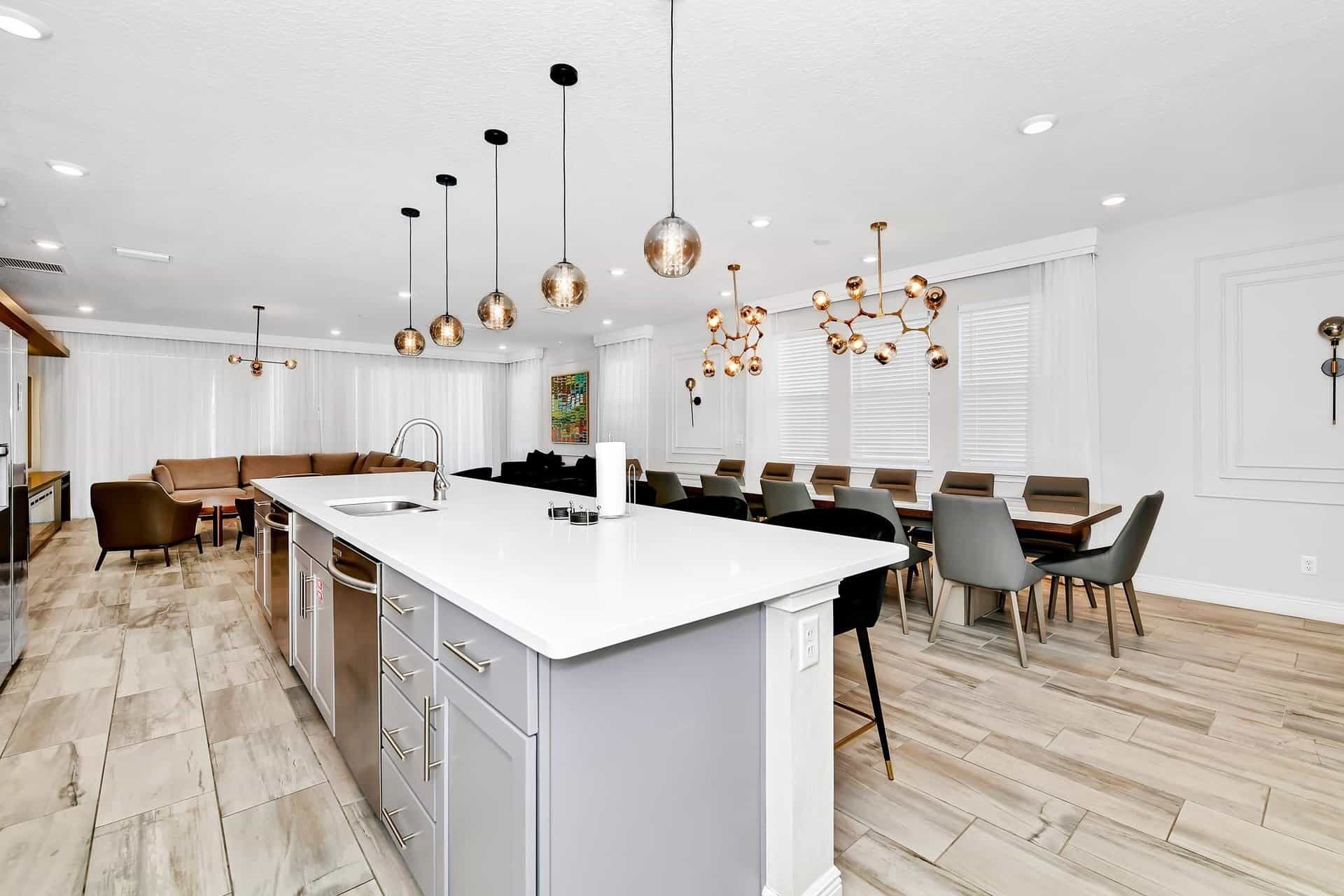 Eine moderne Küche mit Kochinsel, Pendelleuchten und einem Essbereich mit einem langen Tisch.