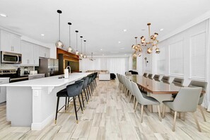 A modern kitchen with a central island, bar stools, and a dining area with a long table and chairs. - UFC Champion José Aldo’s 9-BR Near to Disney (Kissimmee)