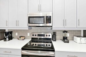 Une cuisine moderne équipée d’appareils électroménagers en acier inoxydable, notamment un four à micro-ondes, une cuisinière et une machine à café.