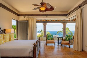 A hotel room with a bed, a ceiling fan, a view of the ocean, and a balcony with chairs. - Stunning 8BR Cabo Villa with Butler & Cooking Services (Cabo San Lucas)