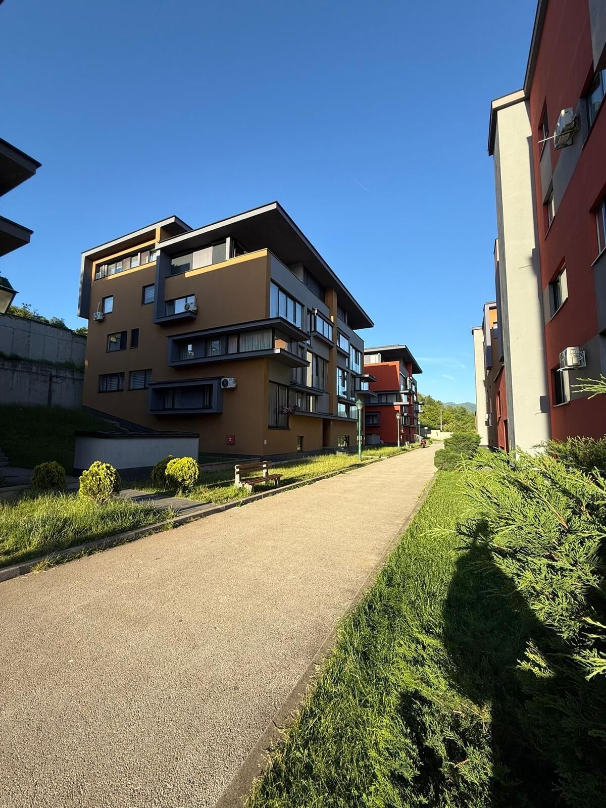 Ein mehrstöckiges Wohngebäude mit Balkonen, einem gepflasterten Weg und Grünflächen an den Seiten.