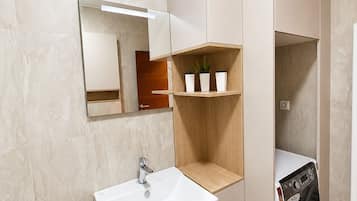 Et moderne badeværelse med en hvid vask, spejl og indbyggede hylder med planter.