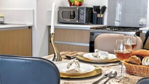 A dining area with a table set for two, a microwave, a stove, and a basket of bread. - Golden Hour 1BR | Creek Beach with Lagoon Access (Dubai)