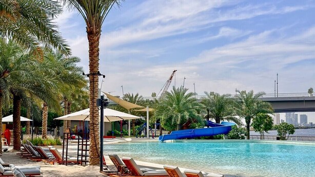 A poolside area with lounge chairs, palm trees, and a water slide. - Golden Hour 1BR | Creek Beach with Lagoon Access (Dubai)