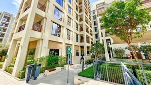 A multi-story residential building with balconies, a gated entrance, and a landscaped area with trees. - Golden Hour 1BR | Creek Beach with Lagoon Access (Dubai)