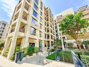 A multi-story residential building with balconies, a gated entrance, and a landscaped area with trees. - Golden Hour 1BR | Creek Beach with Lagoon Access (Dubai)