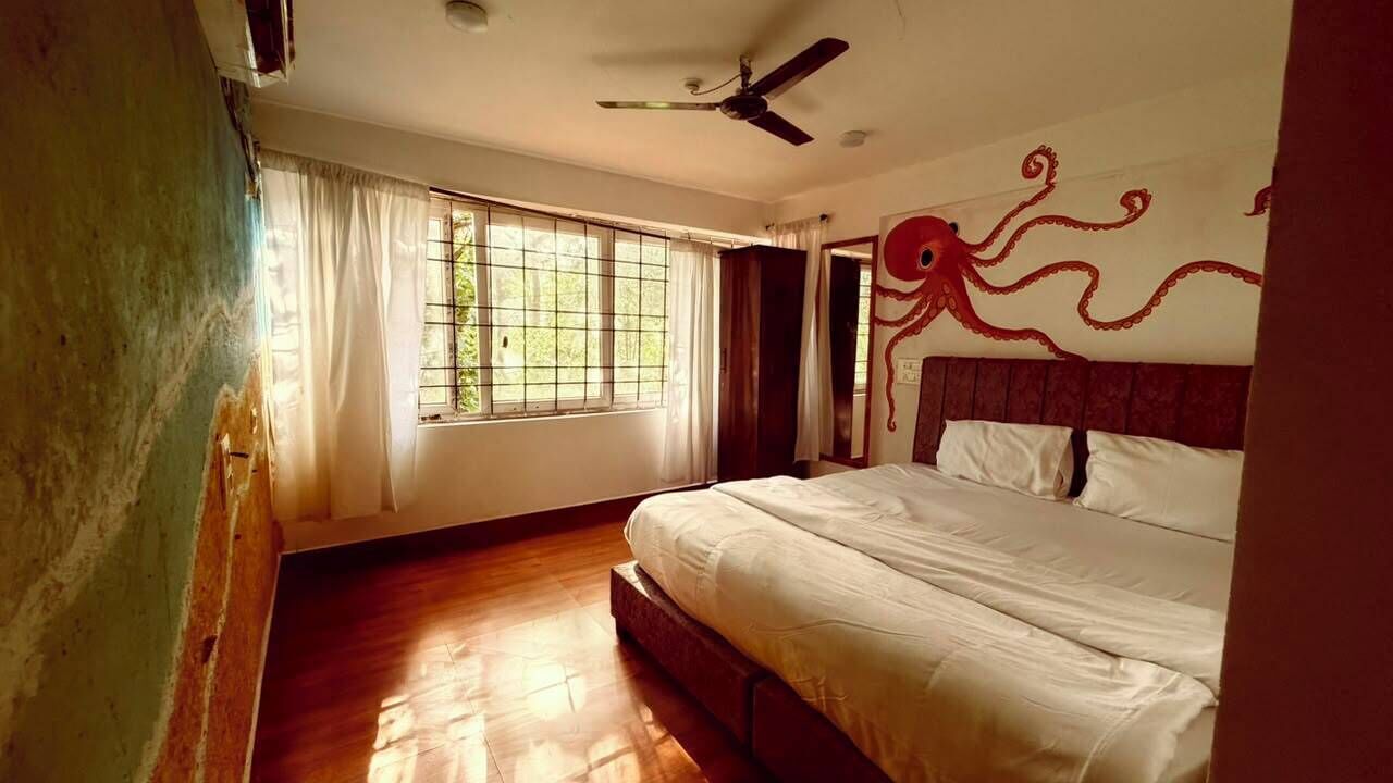 Ein Zimmer mit einem Bett, einem Deckenventilator, einem Fenster mit Vorhängen und einer Wand mit einem roten Oktopus-Design.