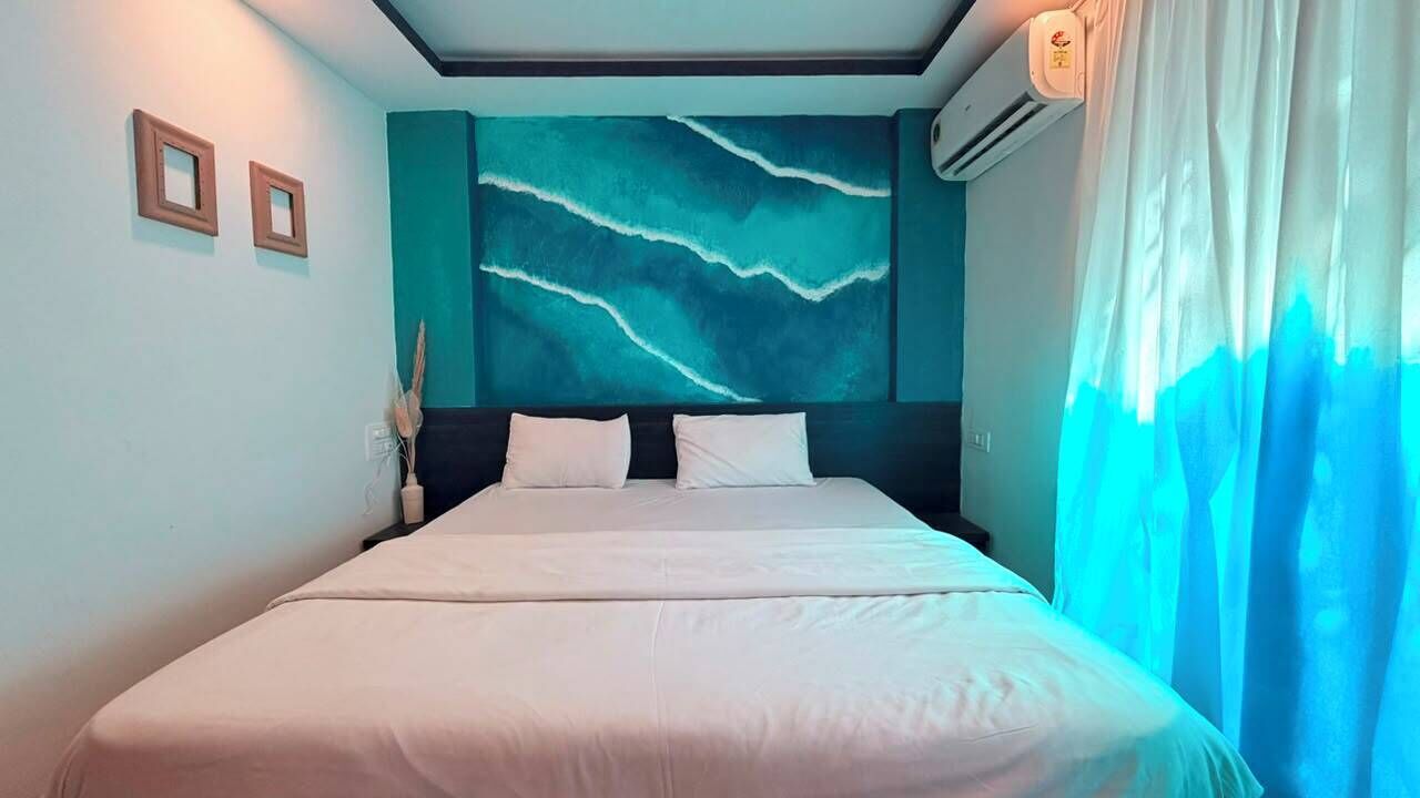 A bed with white bedding, a teal accent wall, and a window with a blue curtain.