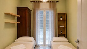 Quarto de hotel com duas camas, um guarda-roupa de madeira, uma estante com uma planta e uma porta com cortina.