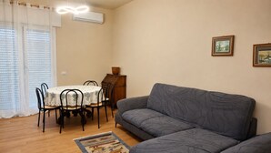 Uma sala de estar com sofá, mesa de jantar e cadeiras, e um pequeno armário.