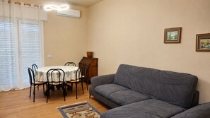Ein Wohnzimmer mit einer Couch, einem Esstisch mit Stühlen und einem kleinen Schrank.