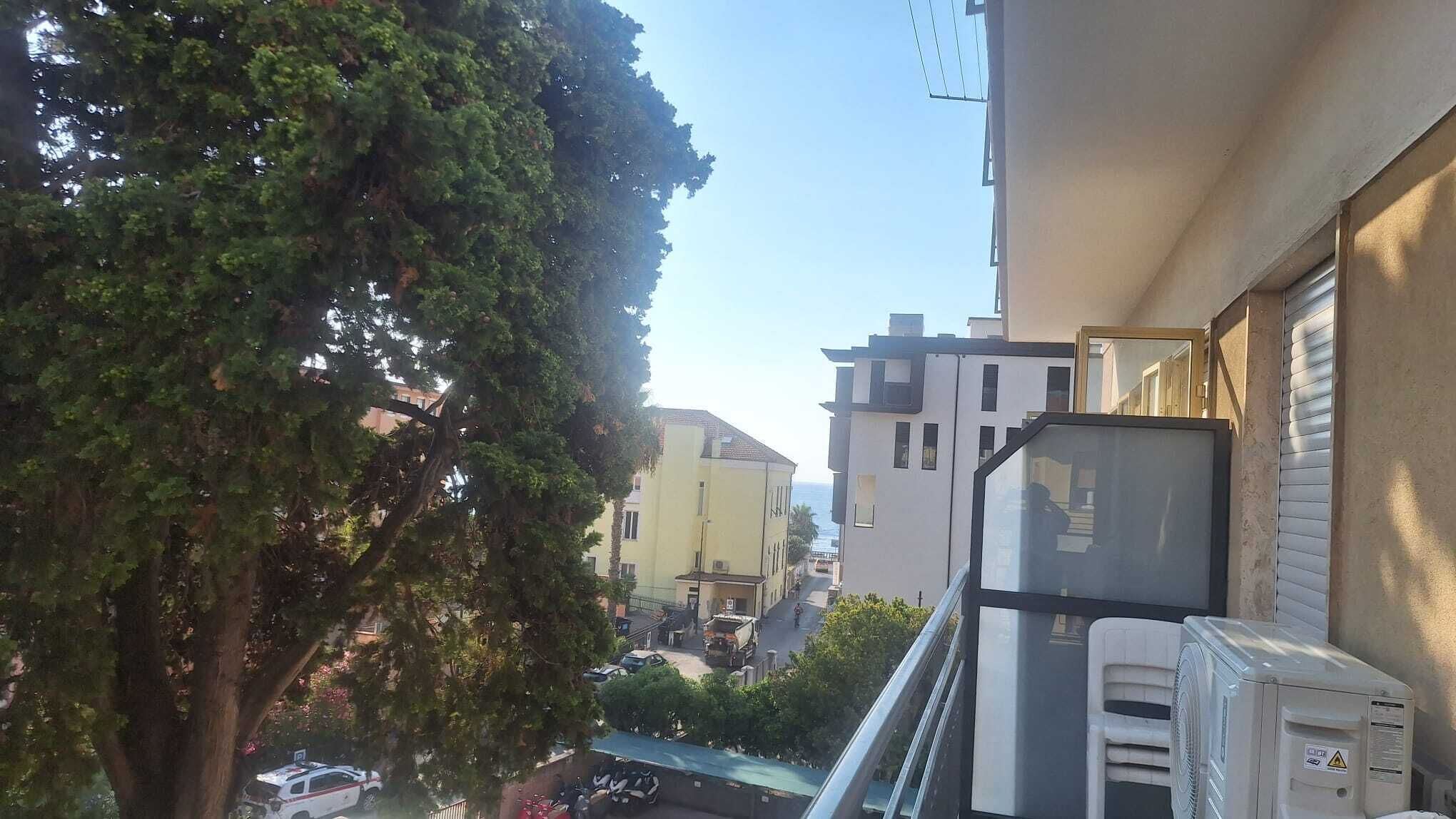 A residential street with buildings, a tree, and parked vehicles.
