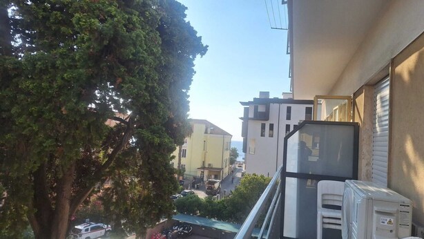Uma rua residencial com edifícios, uma árvore e veículos estacionados.